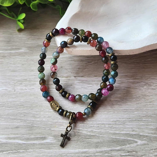 Multicolored beaded bracelet with a cross charm on a wooden surface with greenery in the background
